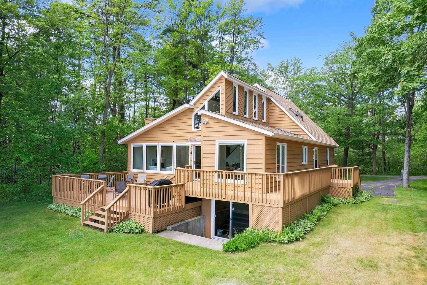 A two-story wooden cabin with a deck, surrounded by trees.