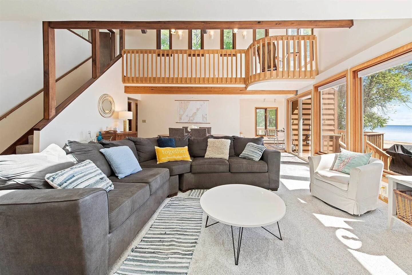 A spacious living area with a large sectional sofa, a white coffee table, and a view of the sea through large windows.