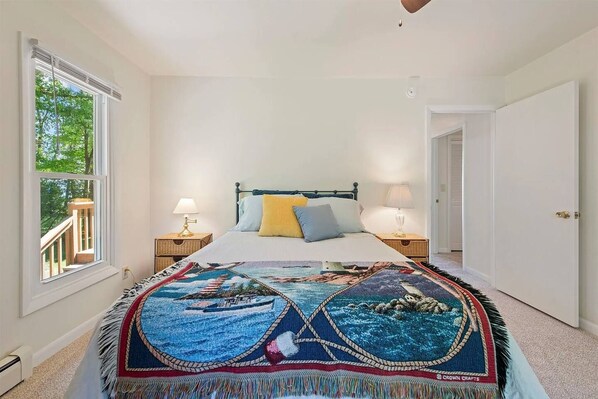 A bedroom with a bed, two bedside tables, a window with a view, and a door.