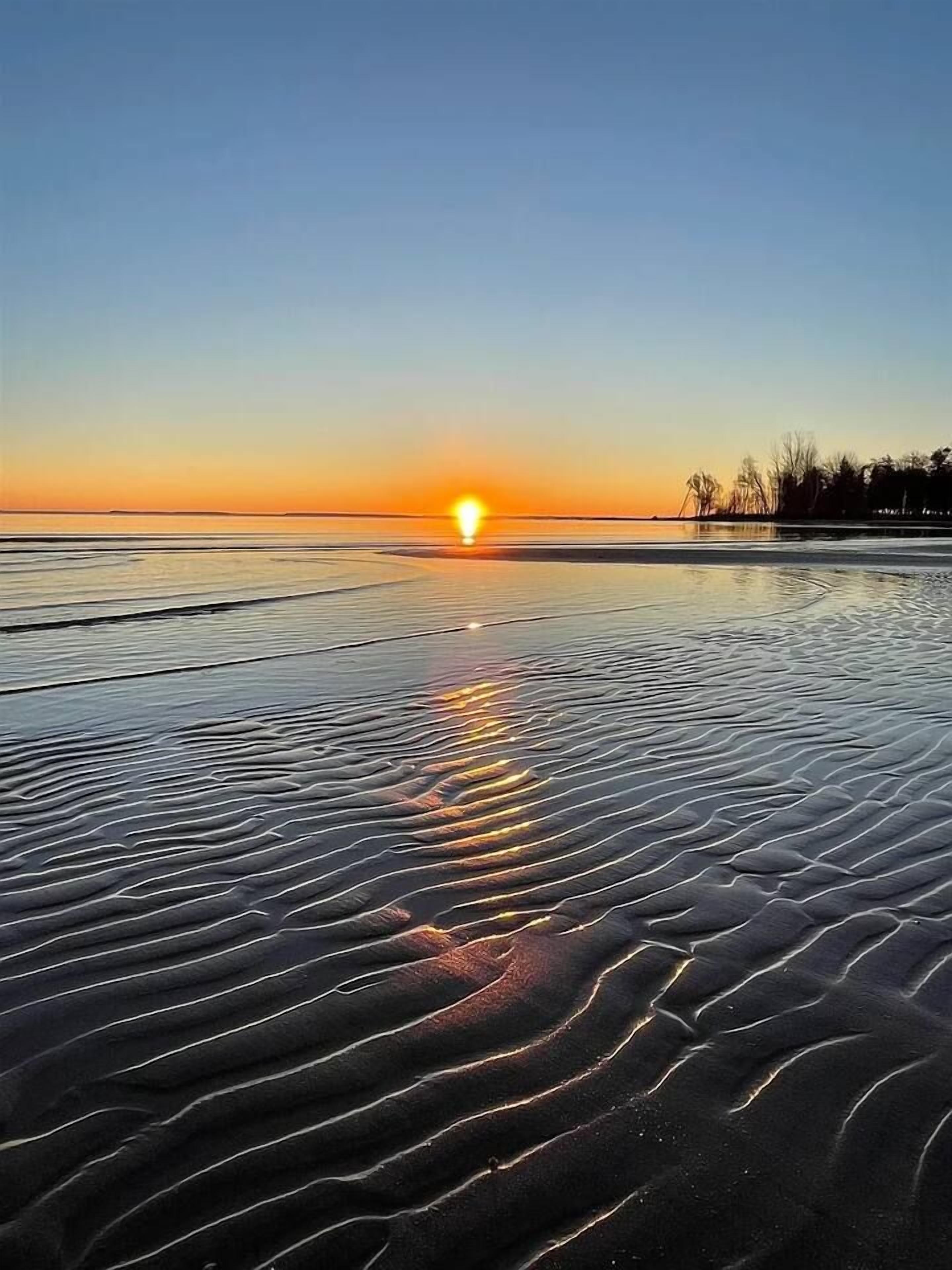 Ranta, jossa on näkyvissä auringonlasku, tyyni vesi ja hienoa hiekkaa, joka on aaltojen muovaamaa.