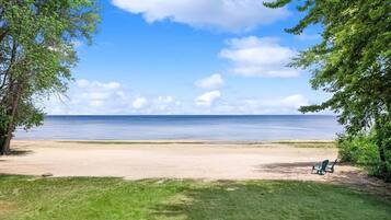 A beach with a clear sky, a sandy shore, and a single green chair.
