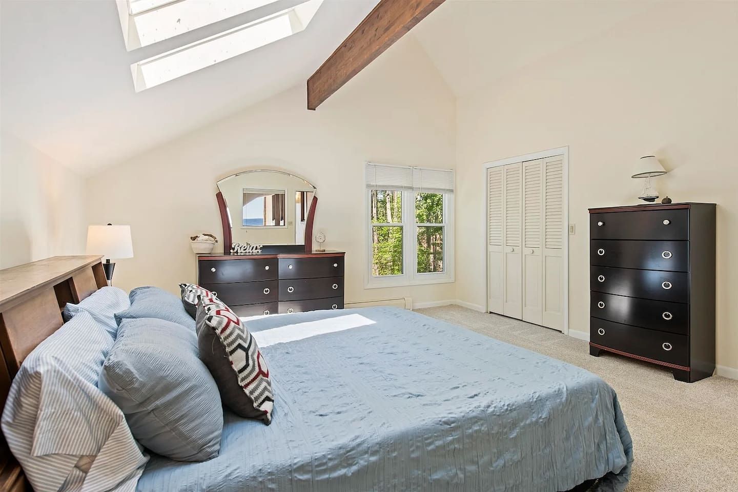 A bedroom with a bed, dresser, mirror, and a window with a view of trees.