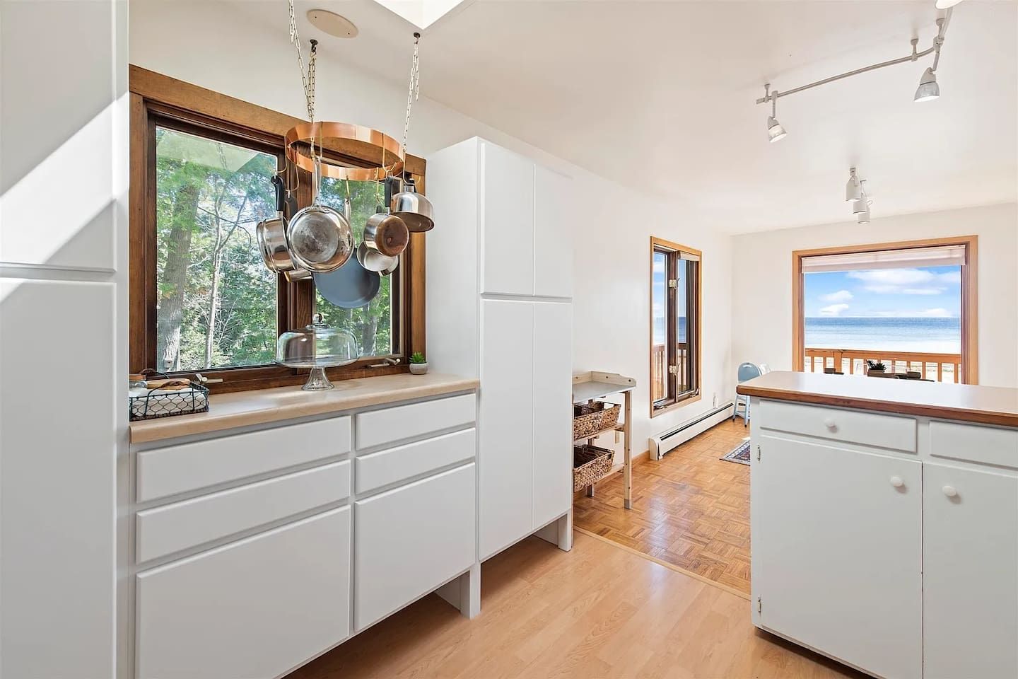 A kitchen with white cabinets, a wooden countertop, and a window with a view of the outdoors.