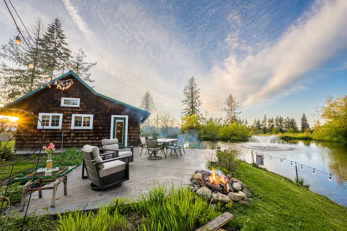 A cabin with a patio, outdoor seating, a fire pit, and a pond.