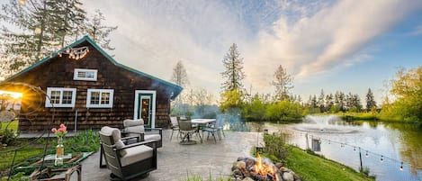 A cabin with a patio, outdoor seating, a fire pit, and a pond.