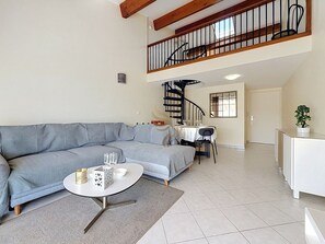 Una sala de estar con un sofá gris, una mesa de centro redonda y una escalera espiral que sube a un nivel superior.