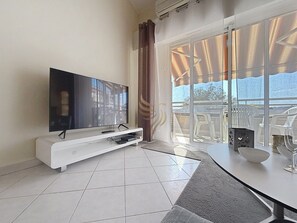 Ein modernes Wohnzimmer mit Flachbildfernseher, einer weißen Unterhaltungsanlage und einem Essbereich mit Tisch und Stühlen.