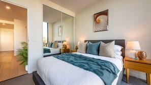 Ein Hotelzimmer mit einem großen Bett, einem Nachttisch, einer Lampe, einem Spiegel und Blick auf den Flur.