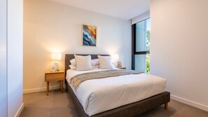 Un dormitorio con una cama, mesitas de noche, una lámpara y un cuadro en la pared.