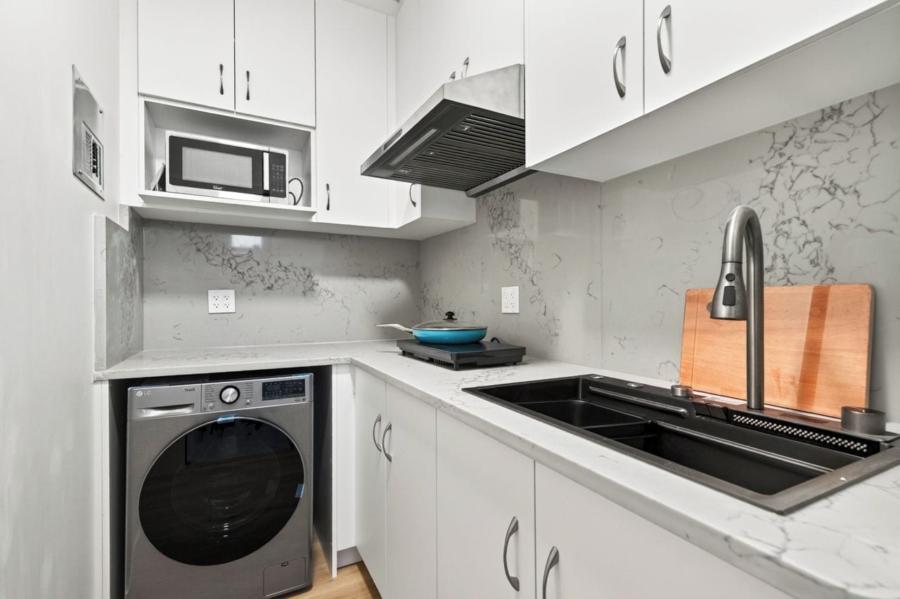 A compact kitchen with a built-in washer, a microwave, and a sink with a modern faucet.