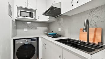 Una cocina compacta con lavadora integrada, microondas y lavabo con grifo moderno.