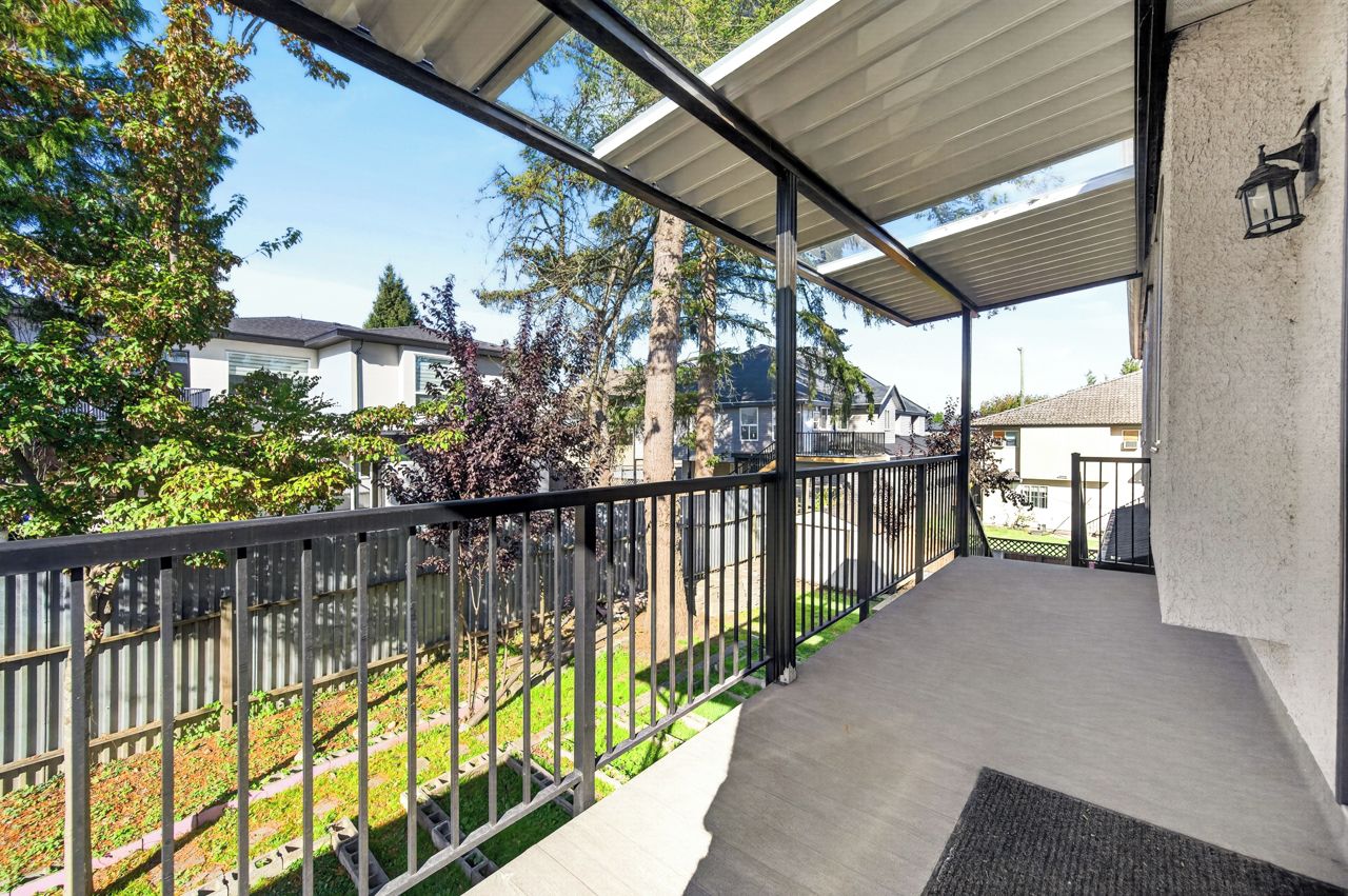 A covered outdoor balcony with a metal railing, a concrete floor, and a view of a residential area with houses and trees.