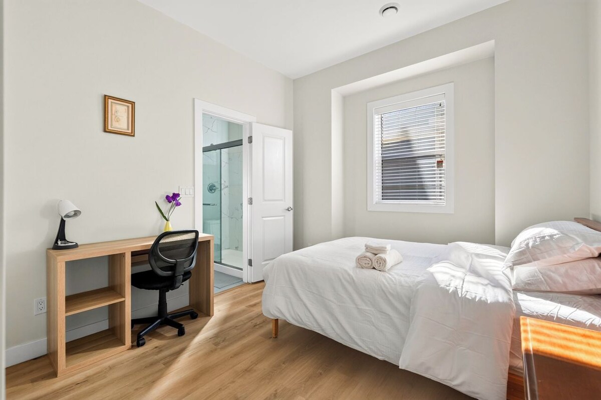 A bedroom with a bed, a desk, a chair, a window, and a door.