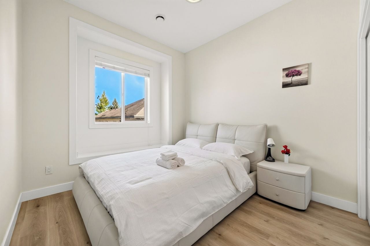 A bedroom with a large bed, a nightstand, a window with a view, and a small picture on the wall.