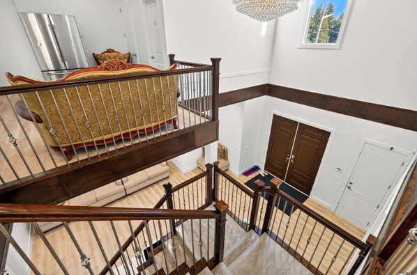 A multi-level interior with a staircase, a bed with a patterned bedspread, a chandelier, and a door.