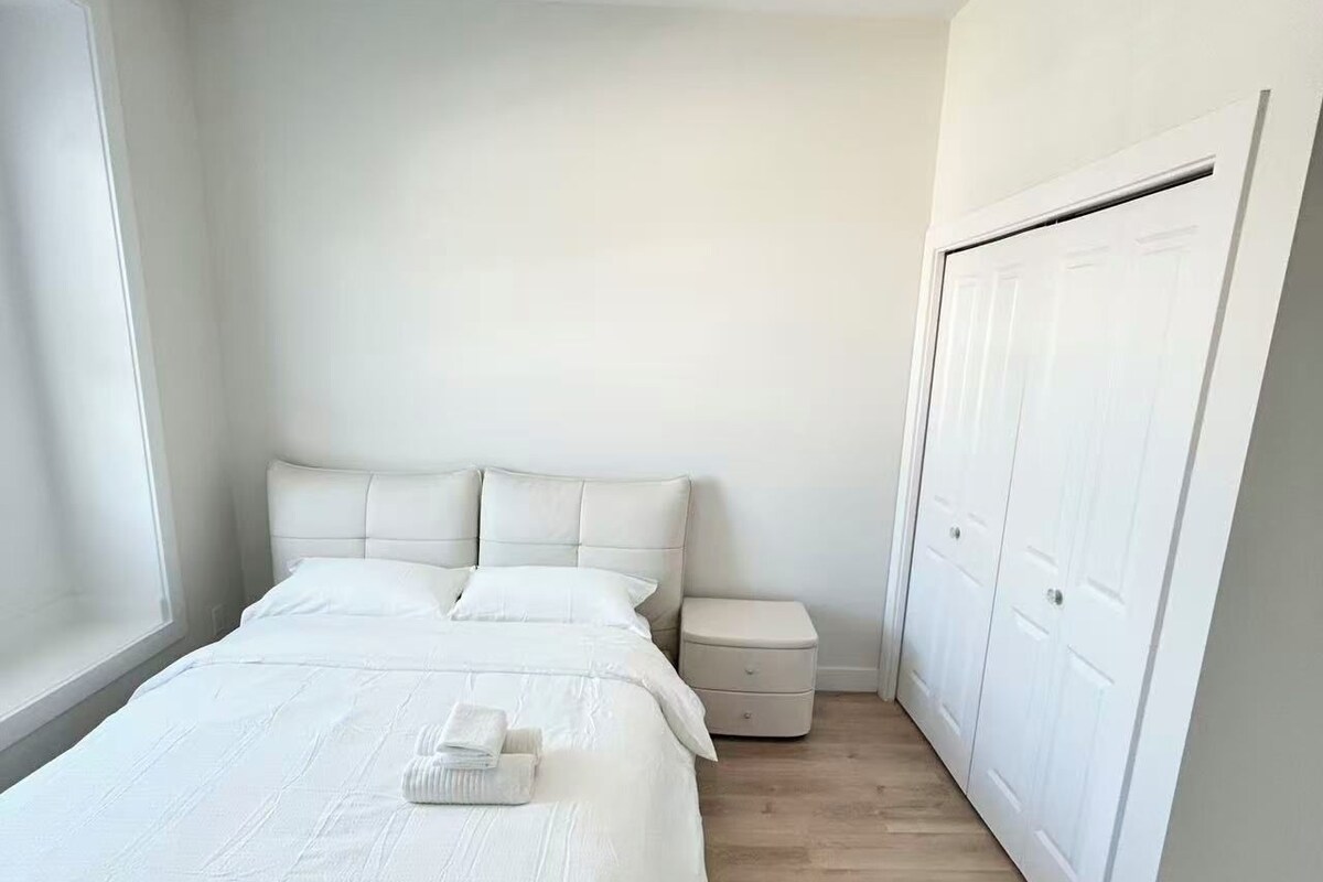 Ett sovrum med en säng, sängbord, en garderob och ett fönster.