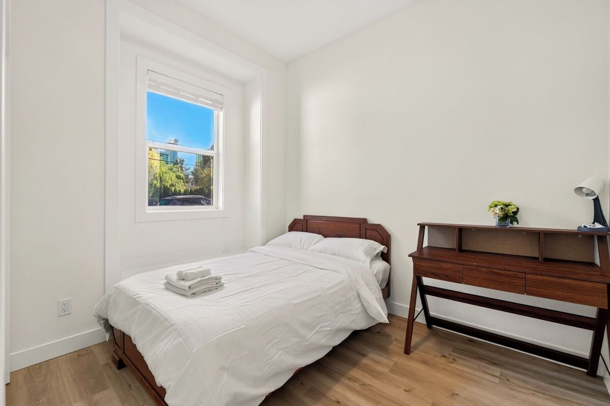 A bedroom with a bed, a desk, and a window.