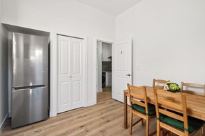 A modern kitchen with a stainless steel refrigerator, white double doors, and a wooden dining table with chairs.