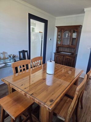 A dining area with a wooden table and chairs, a cabinet with glass doors, and a refrigerator. - Stay Cozy Orchard (Clarington)