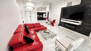 Un salon moderne avec un canapé en cuir rouge, une table basse en verre et un téléviseur à écran plat fixé sur un mur noir et blanc.