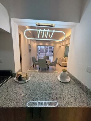 A modern kitchen with granite countertops, a dining area with a table and chairs, and a view of the outside through a sliding door. - MOONLIGHT APARTMENT NEAR THE BEACH (Puerto Plata)