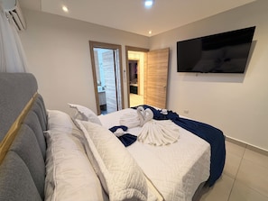 Ein Hotelzimmer mit einem Bett, einem an der Wand befestigten Fernseher und einer offenen Tür zu einem Badezimmer.