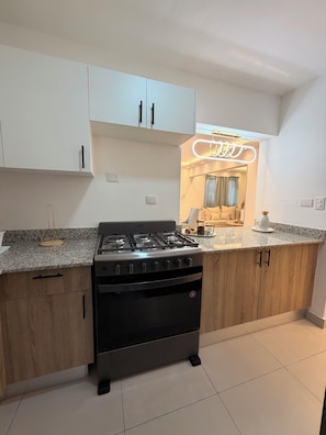 A modern kitchen with a gas stove, wooden cabinets, and a countertop. - MOONLIGHT APARTMENT NEAR THE BEACH (Puerto Plata)