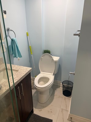 A bathroom with a toilet, a sink, a mop, and a trash bin. - Unique and peaceful. (Whitby)