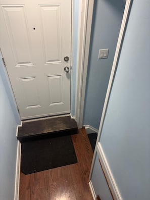 A hallway with a white door, a black doormat, and a light blue wall. - Unique and peaceful. (Whitby)