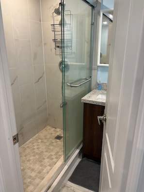 A glass-enclosed shower with a metal rack, a sink with a soap dispenser, and a wooden cabinet. - Unique and peaceful. (Whitby)