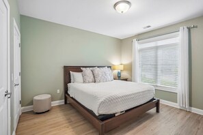 Quarto com cama, luminária de cabeceira e janela com persianas.