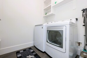 Ein Waschraum mit zwei weißen Waschmaschinen mit Frontlader, einem schwarz-weißen Teppich und einem kleinen Regal über den Maschinen.