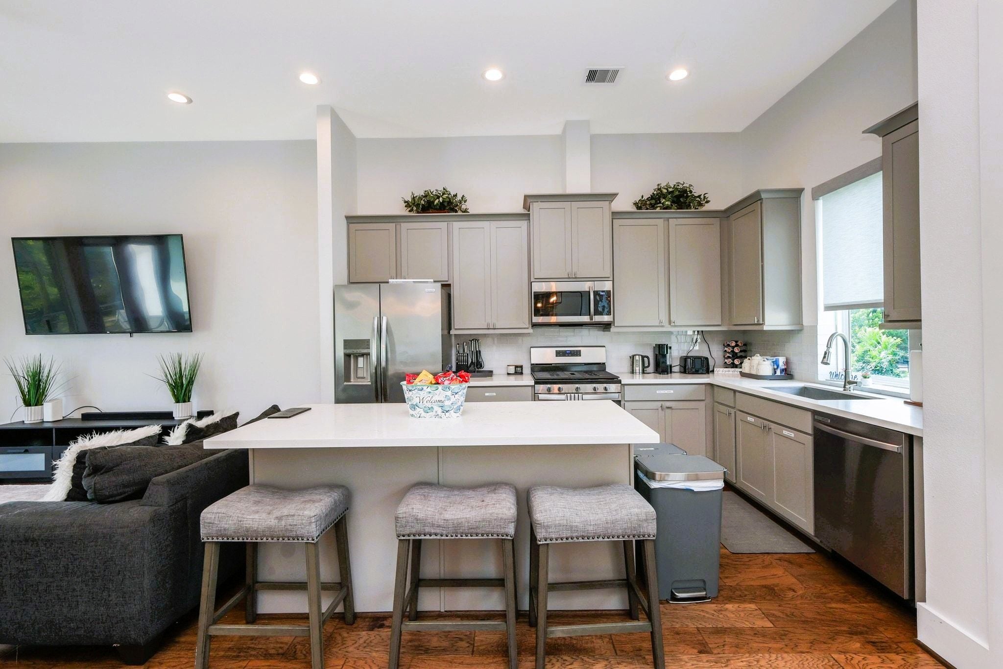 A modern kitchen with a central island, bar stools, a built-in oven, and a large window.