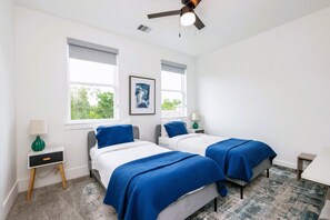 Ein Schlafzimmer mit zwei Betten, einem Deckenventilator und einem Fenster mit Blick auf Grünflächen.