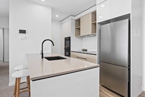 A modern kitchen with a stainless steel refrigerator, a built-in oven, and a minimalist design. - Luxurious Beachfront Retreat in Burleigh Heads (Gold Coast)