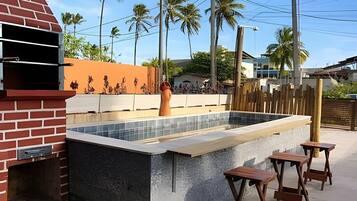 Un espace piscine agrémenté d’une structure en briques, d’une piscine carrelée et de tabourets en bois.