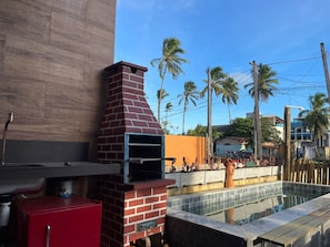 Un horno de ladrillo al aire libre junto a una piscina, con un armario rojo y una fuente de agua cerca.