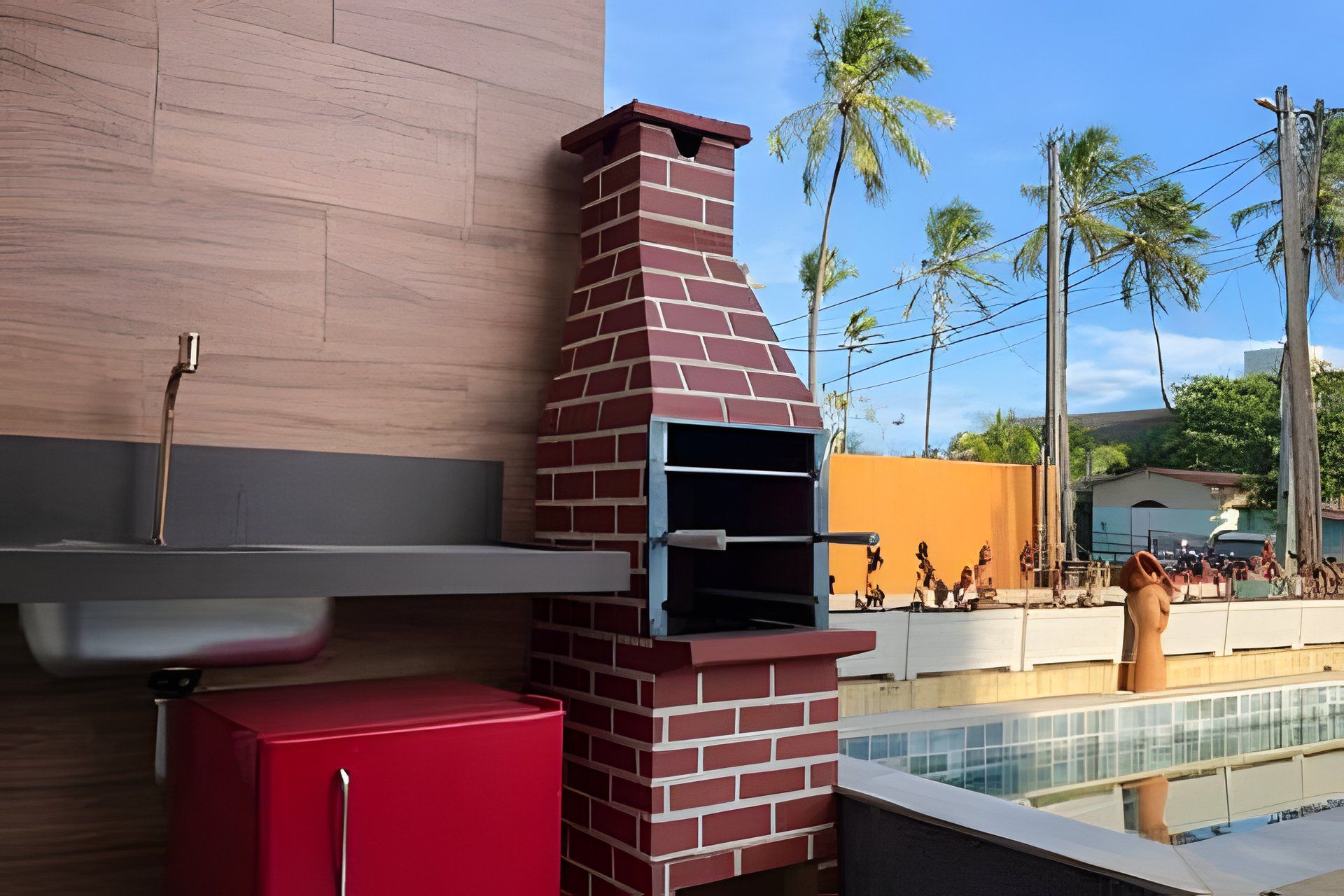 Un barbecue extérieur en briques, doté d’une étagère en métal au-dessus, d’une armoire rouge et d’une piscine en arrière-plan.