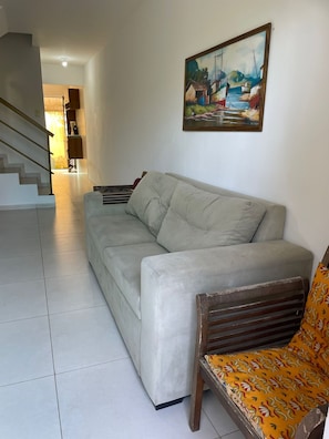 Un saló amb un sofà, una cadira de fusta, un quadre a la paret i una escala que condueix a una altra habitació.