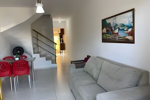 A modern living room with a grey sofa, a dining area with red chairs, and a staircase leading to another room. - Porto de Galinhas Maraca 70m Mar Loctemp (Ipojuca)
