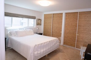 Ein Schlafzimmer mit einem Bett, einem Nachttisch, einer Lampe, einem Kleiderschrank und einem Fenster mit Jalousien.