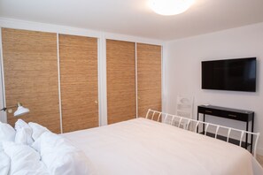 A bedroom with a bed, a bedside lamp, a TV, and a desk with a chair. - Steps to the Sand: Mid-Century 2BR with Ocean-View Patio by Venice Pier (Marina del Rey)