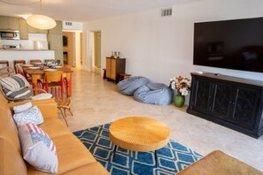A living room with a sofa, a coffee table, a TV, and a dining area with chairs and a table. - Steps to the Sand: Mid-Century 2BR with Ocean-View Patio by Venice Pier (Marina del Rey)