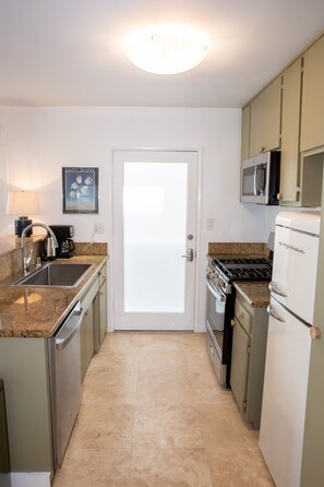 A compact kitchen with a sink, stove, microwave, and cabinets. - Steps to the Sand: Mid-Century 2BR with Ocean-View Patio by Venice Pier (Marina del Rey)