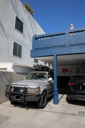 Ein silberner SUV steht in einer Garage mit einer blauen Markise. Im Hintergrund ein schwarzer SUV und ein Gebäude mit einem markanten architektonischen Design.
