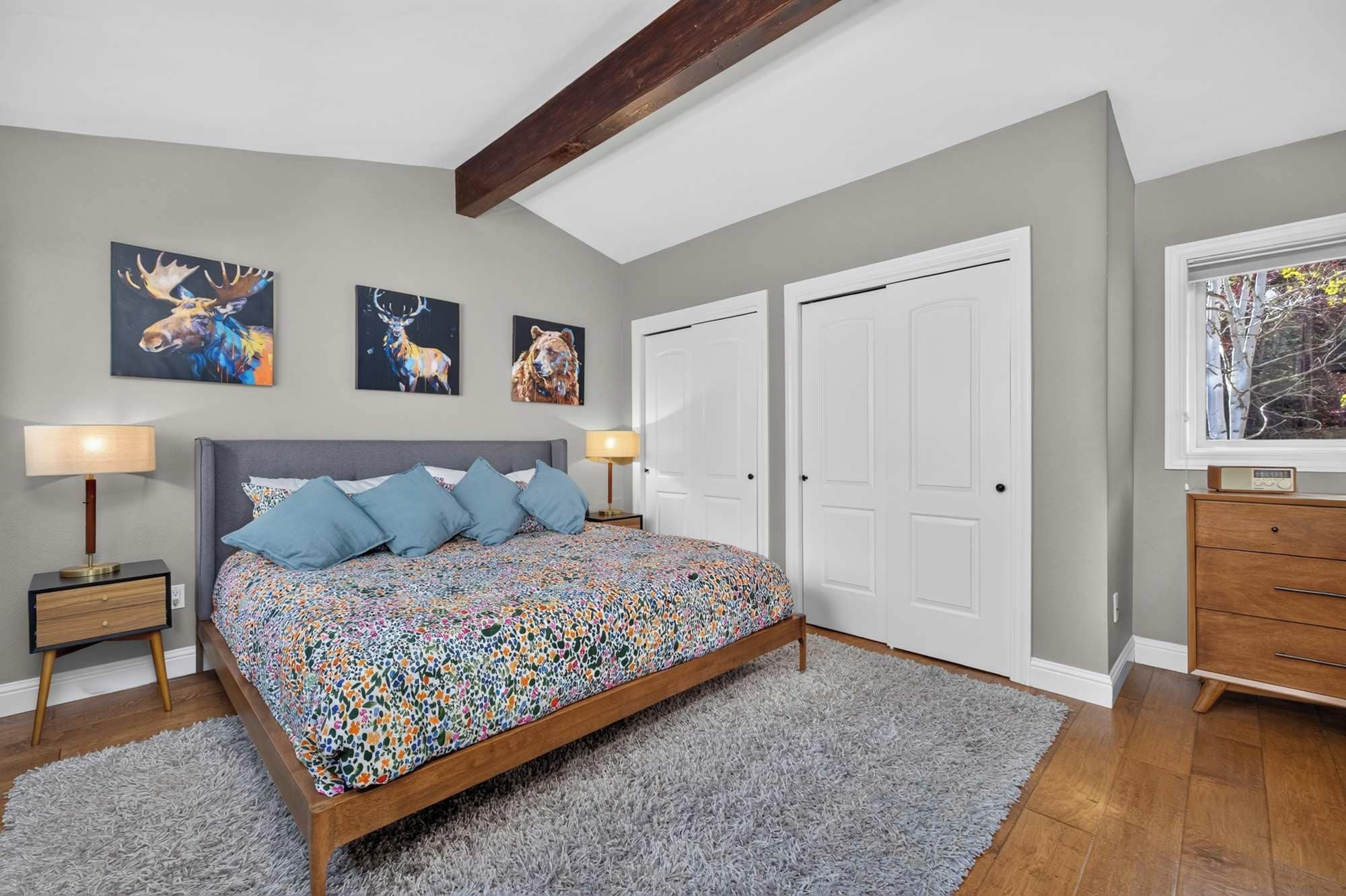 Une chambre à coucher comprenant un lit, deux tables de chevet, une commode, une fenêtre et trois tableaux accrochés au mur.