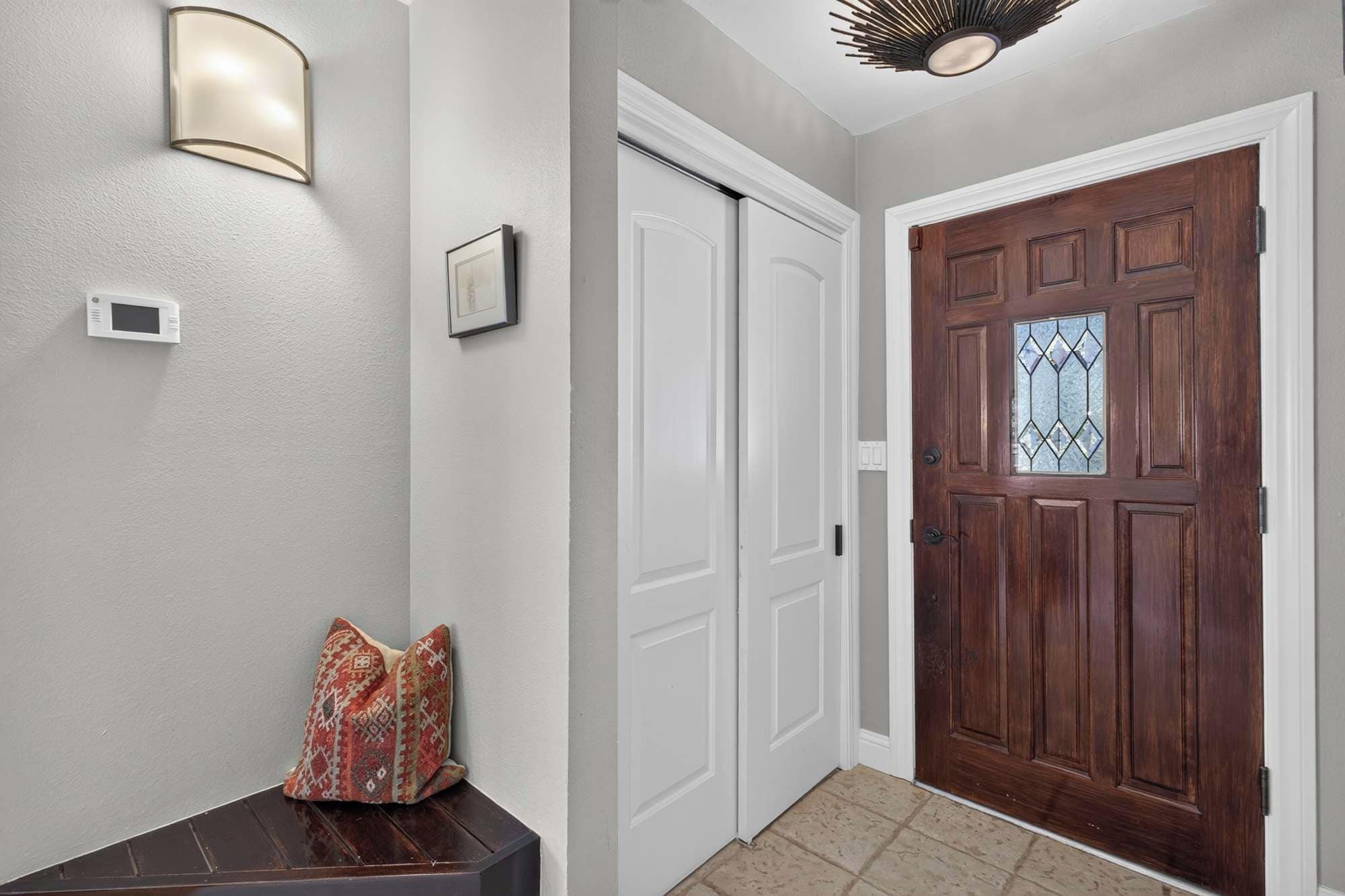 Un couloir avec une porte blanche, un luminaire fixé au mur et un thermostat.