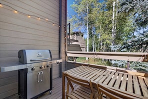 An outdoor deck with a built-in grill, wooden table, and chairs.