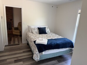 Un dormitorio con cama, una silla y vista a una chimenea de ladrillo.