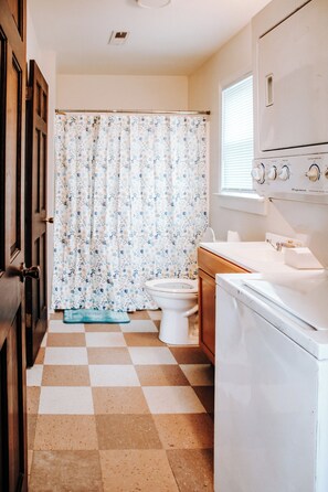 A bathroom with a checkered floor, a toilet, a shower curtain, and a white washing machine. - Welcoming 1-bedroom Apartment in Hayden (Hayden)